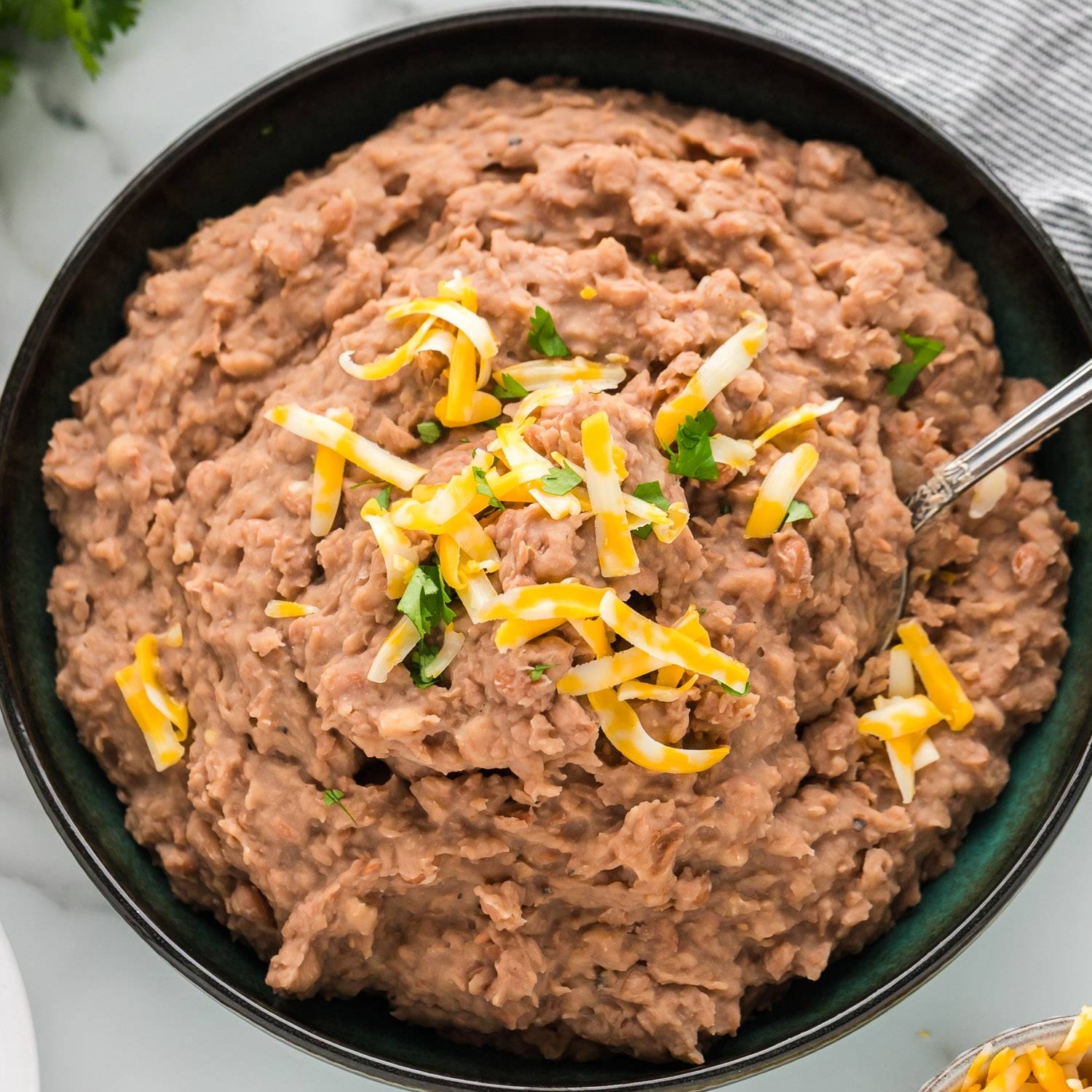 Refried beans topped with cheddar cheese, in a black bowl.