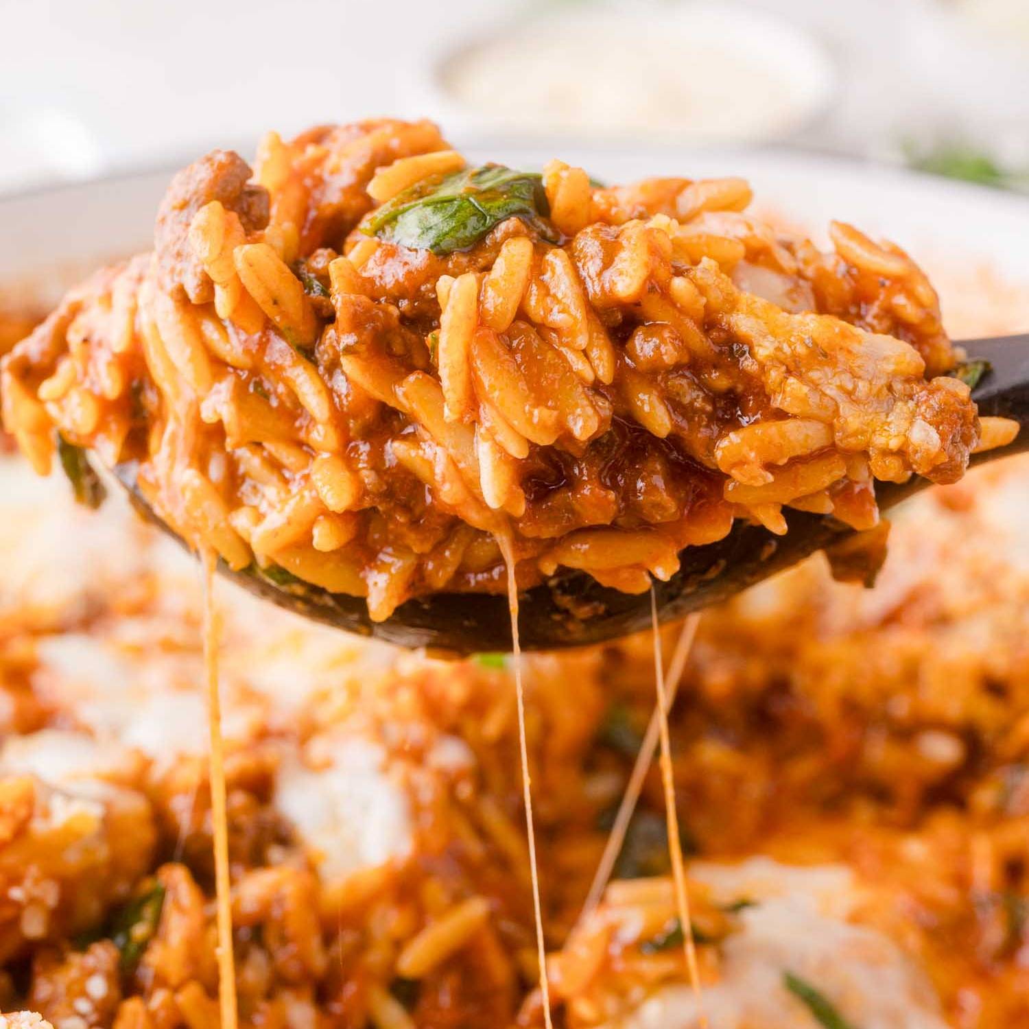 Baked orzo with melted cheese, being scooped out of a pan.