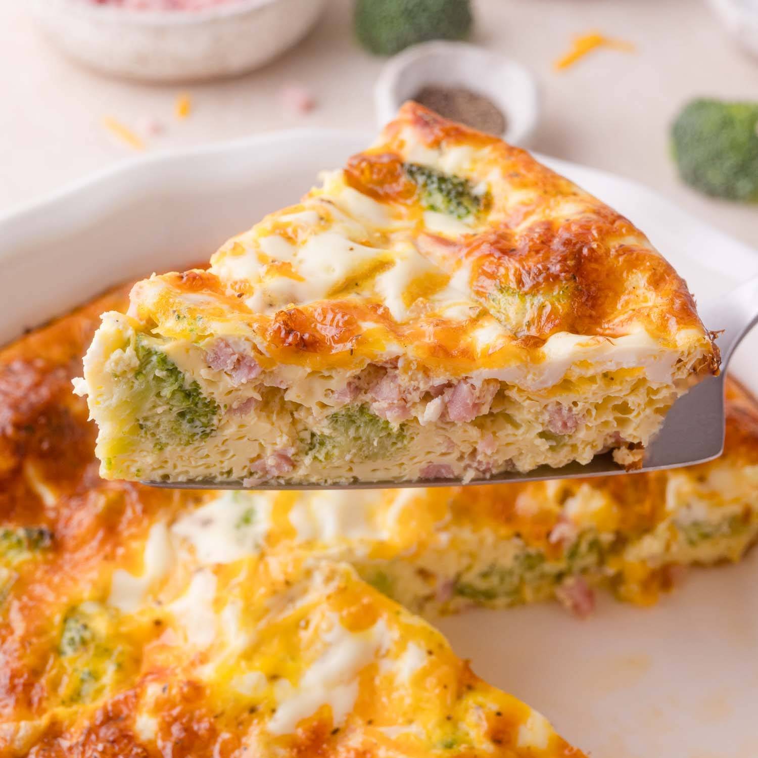 Slice of crustless quiche with ham and broccoli being lifted from a baking dish.