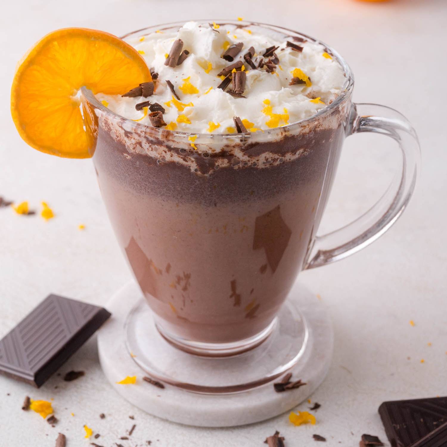 Orange hot chocolate in a clear mug topped with whipped cream.