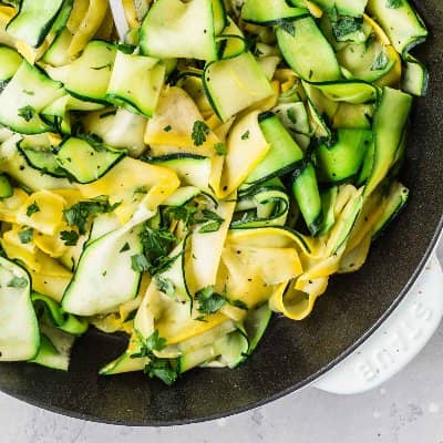 Zucchini and summer squash ribbons in a black skillet, sprinkled with herbs.