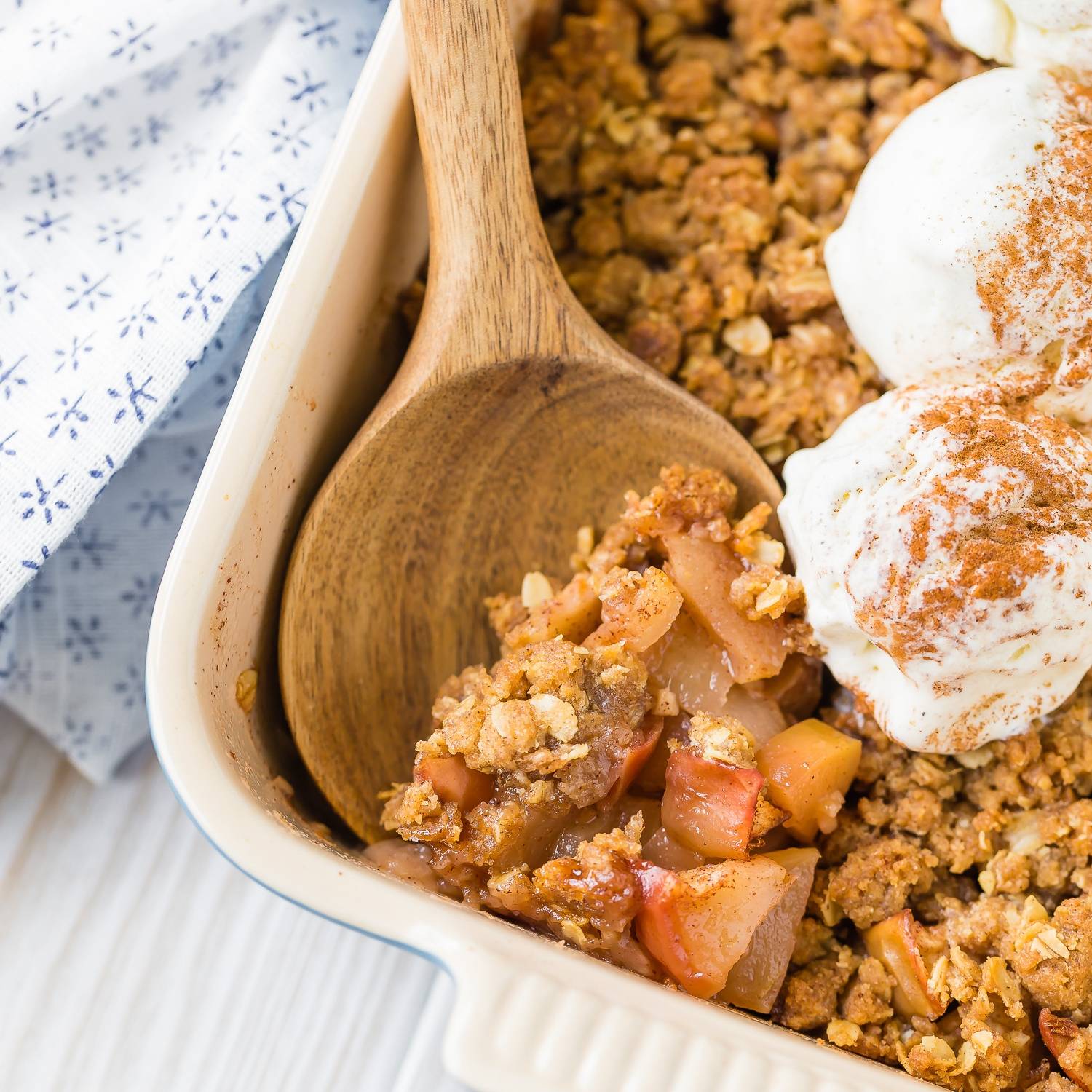 Apple crisp, topped with vanilla ice cream, being scooped out with a large wooden spoon.