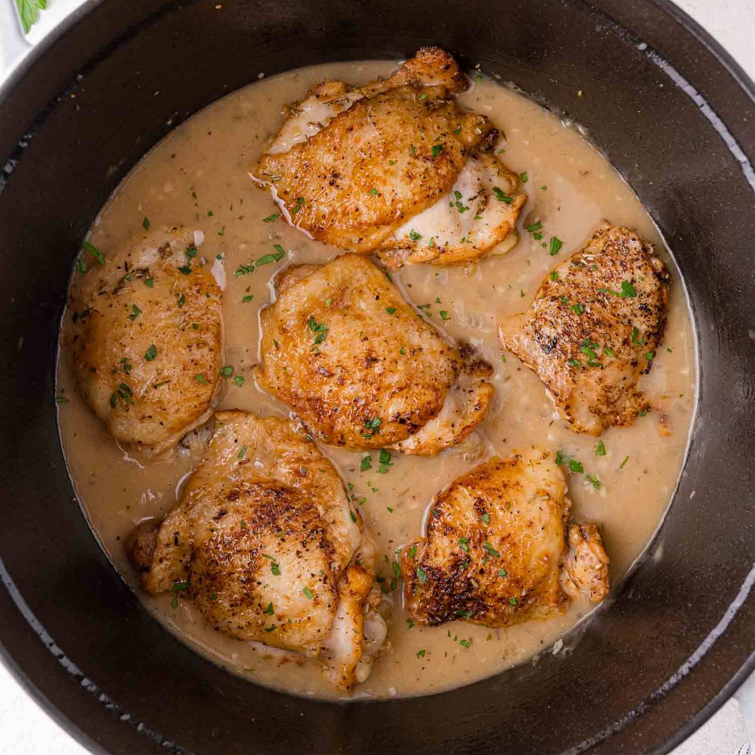 Braised chicken thighs in gravy, in a black pot.