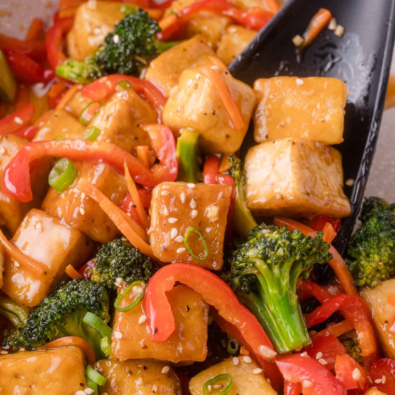 Stir fry with cubes of tofu, broccoli, red bell pepper, carrots, and a light brown sauce.