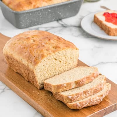 Loaf of whole wheat bread on a wooden cutting board, partially sliced.