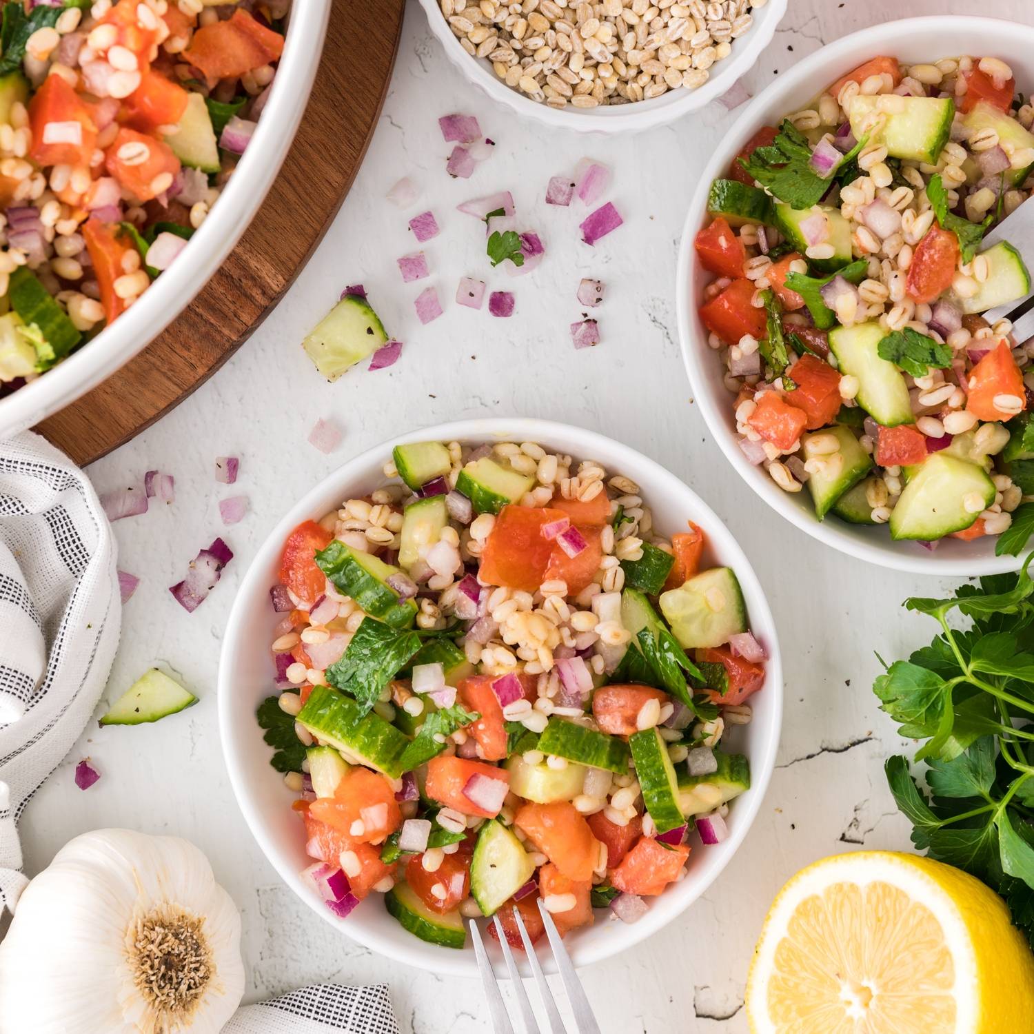 Overhead view of three bowls of barley salad, with tomatoes, onions, parsley, and cucumbers.
