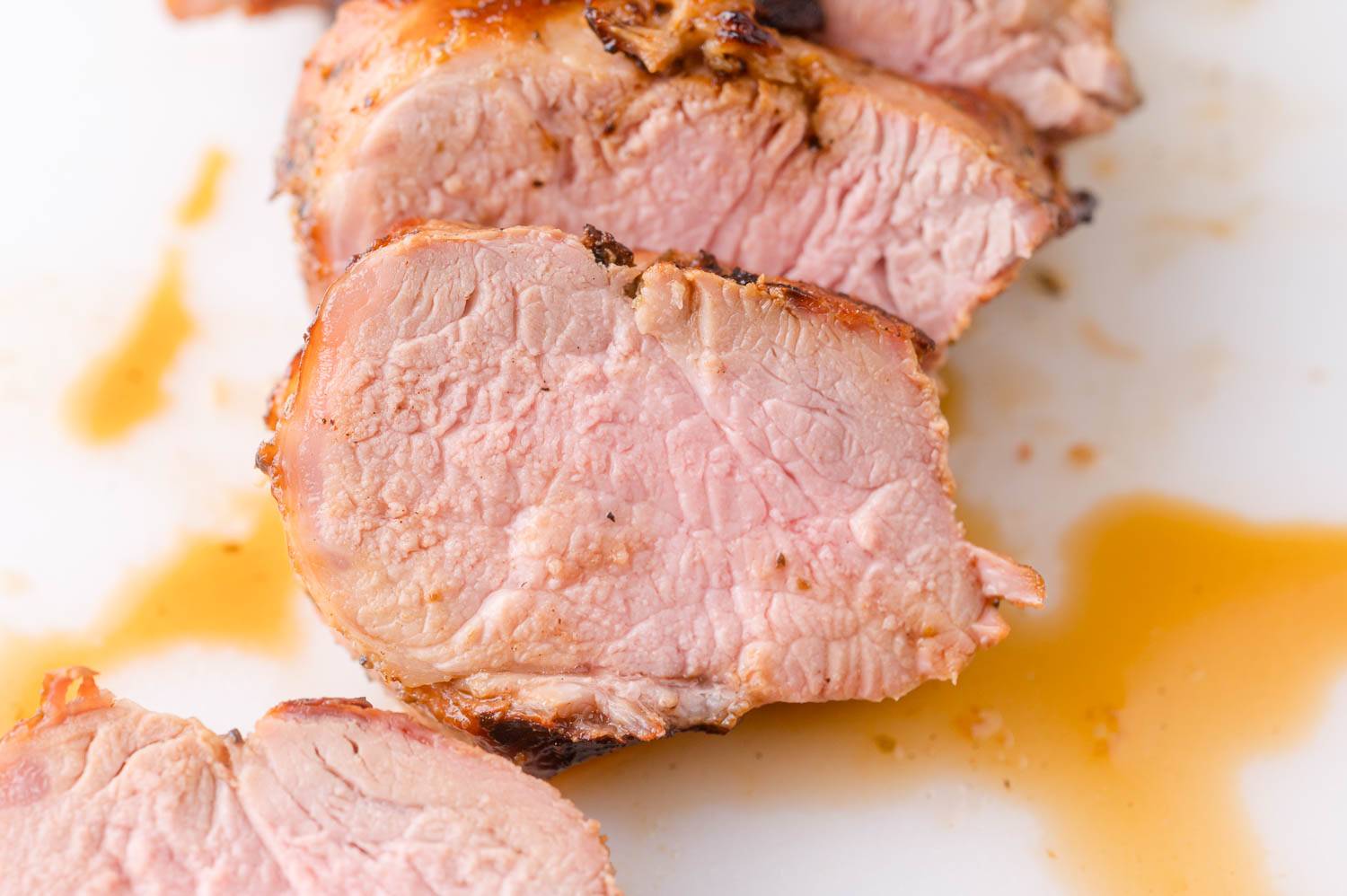 Sliced grilled pork tenderloin, with pools of juice present.
