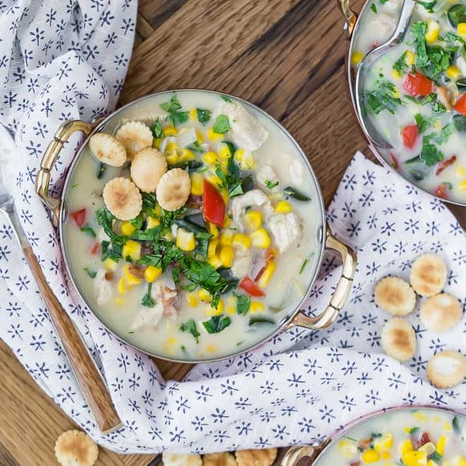 Corn chowder in a metal bowl on a white surface.