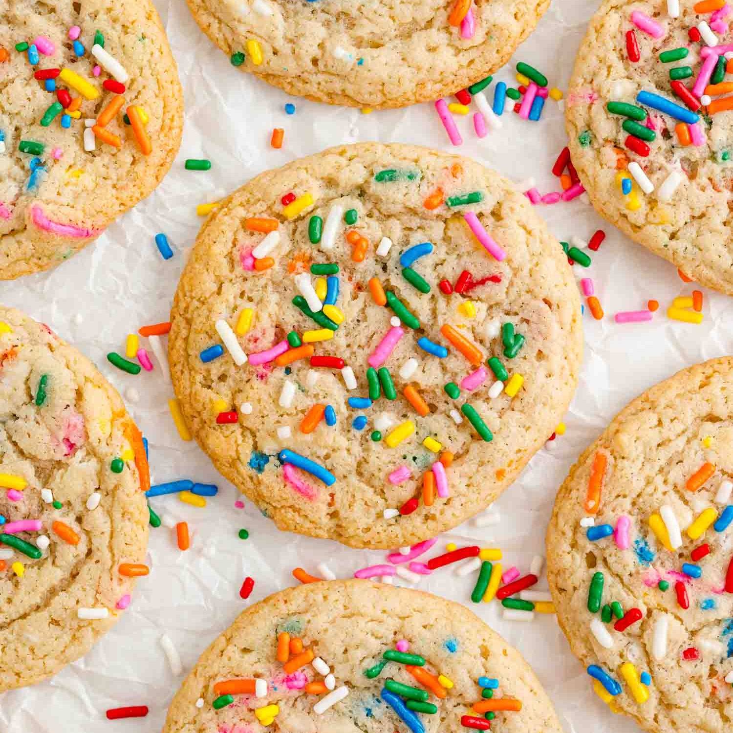 Funfetti cookies on a white surface surrounded by extra sprinkles.