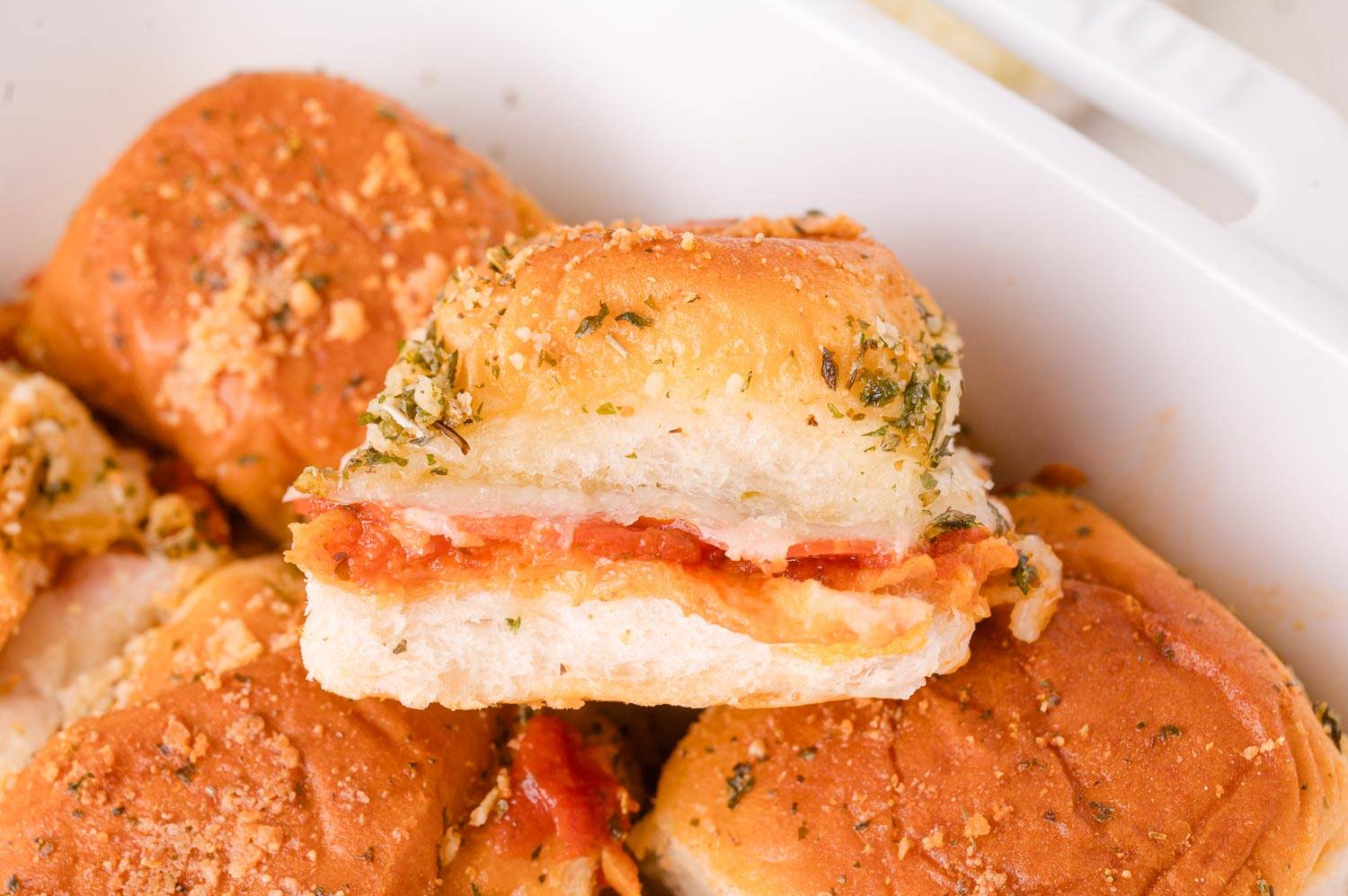 Pizza slider stacked on others in a white baking dish.