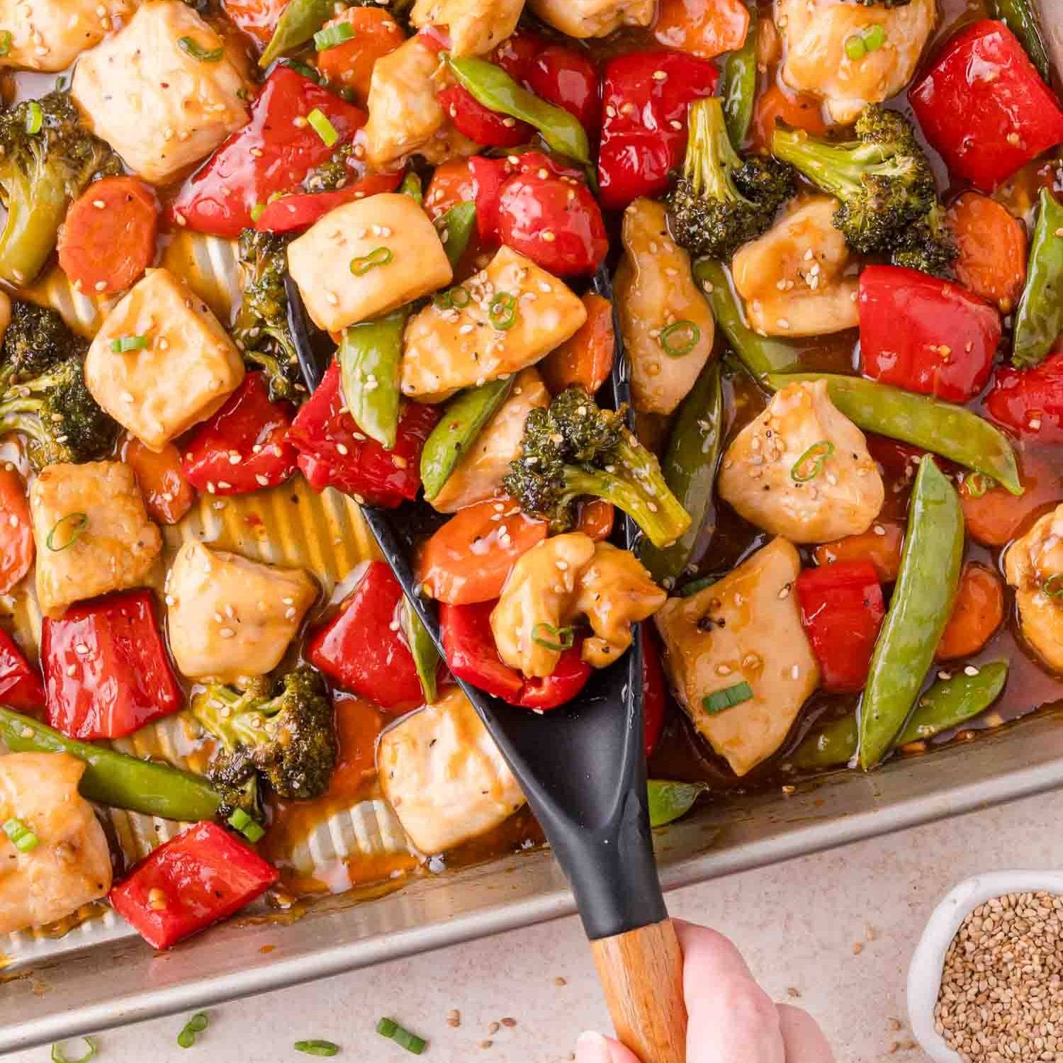 Sheet pan with cubes of chicken, red onions, carrots, broccoli, sugar peas, and a teriyaki sauce.