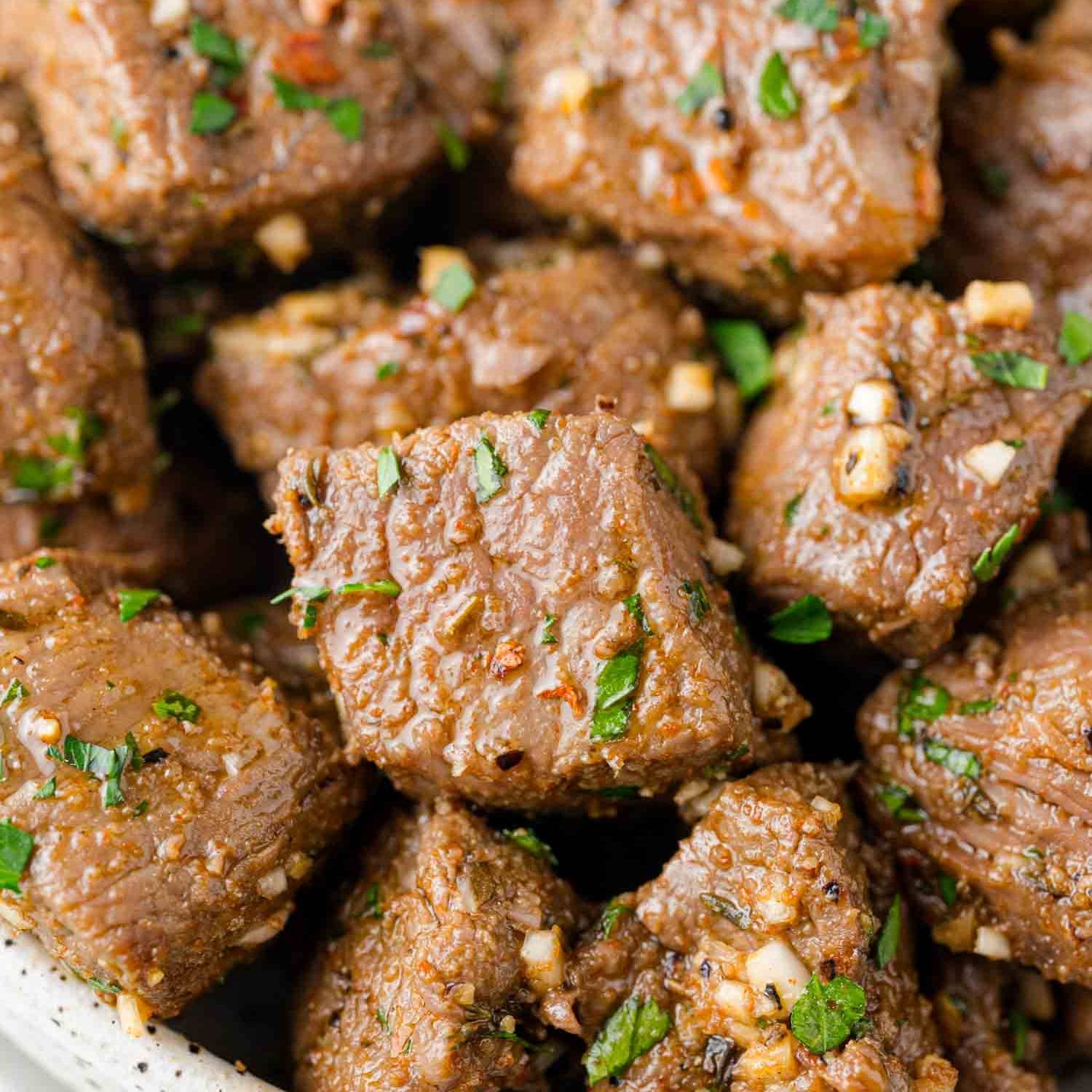 Close up of air fryer steak bites with parsley and minced garlic.