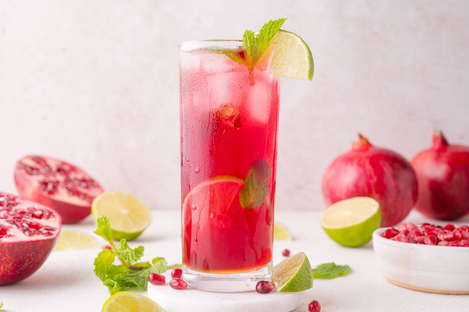 Pomegranate mojito in a tall glass garnished with lime and fresh mint.