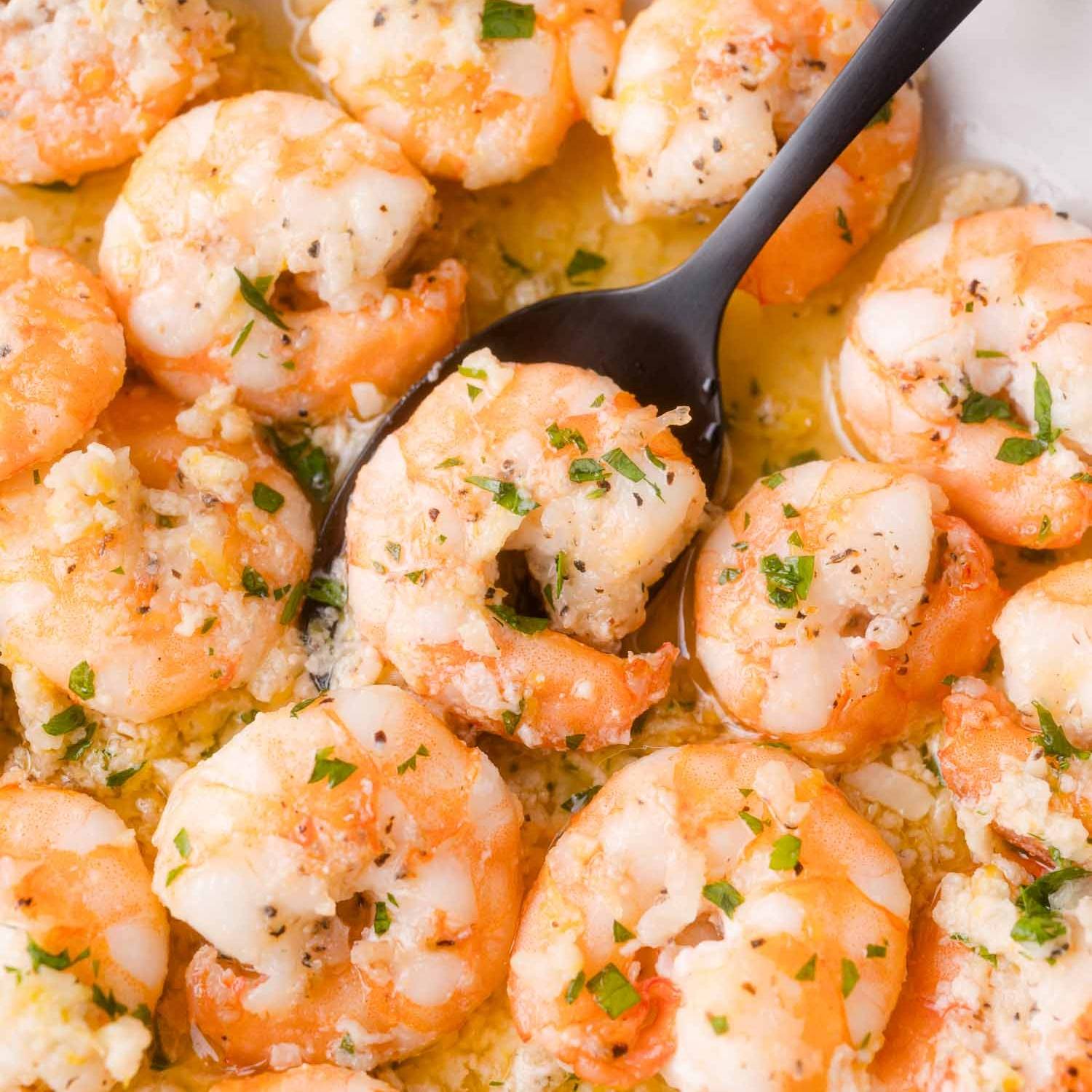 Shrimp with garlic and parsley, with a black spoon scooping it.