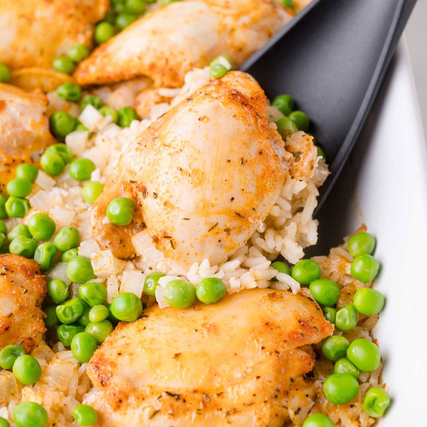 Chicken thigh, rice, and peas being scooped out of baking dish.