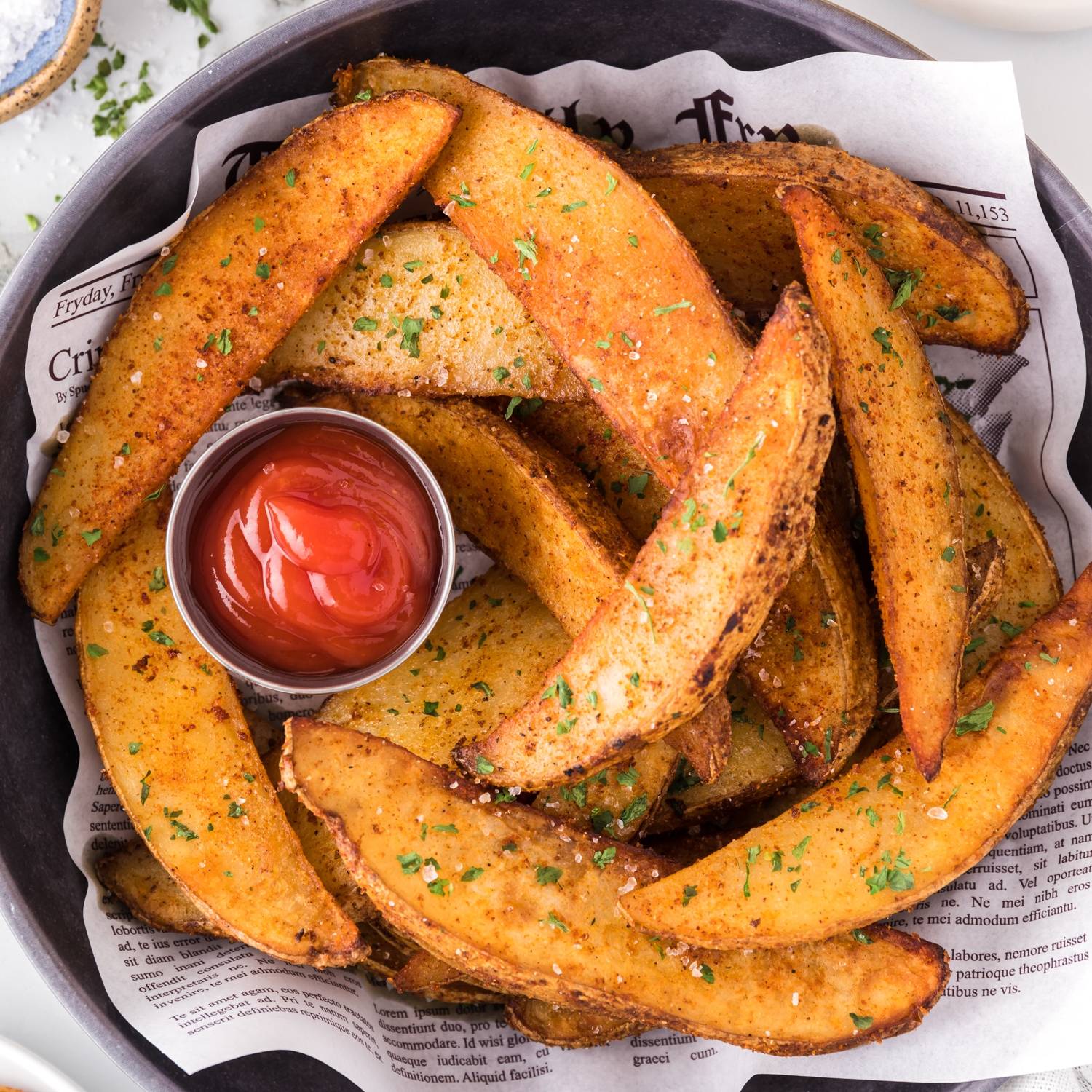 Potato wedges in a basket with a small cup of ketchup.
