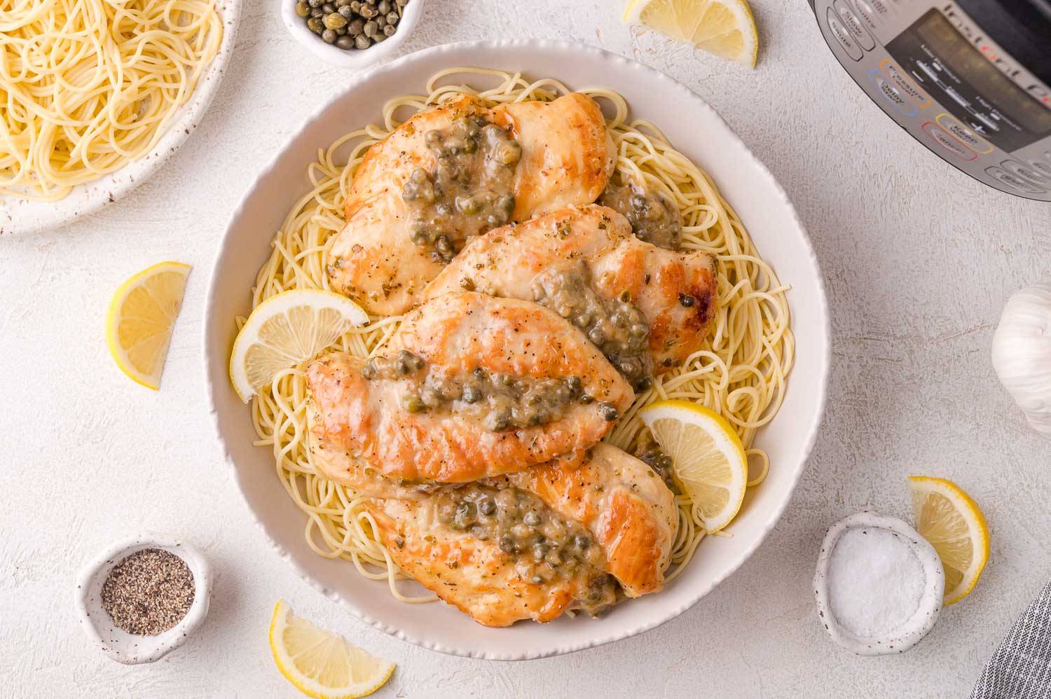 Four pieces of chicken piccata on a plate with angel hair pasta. 