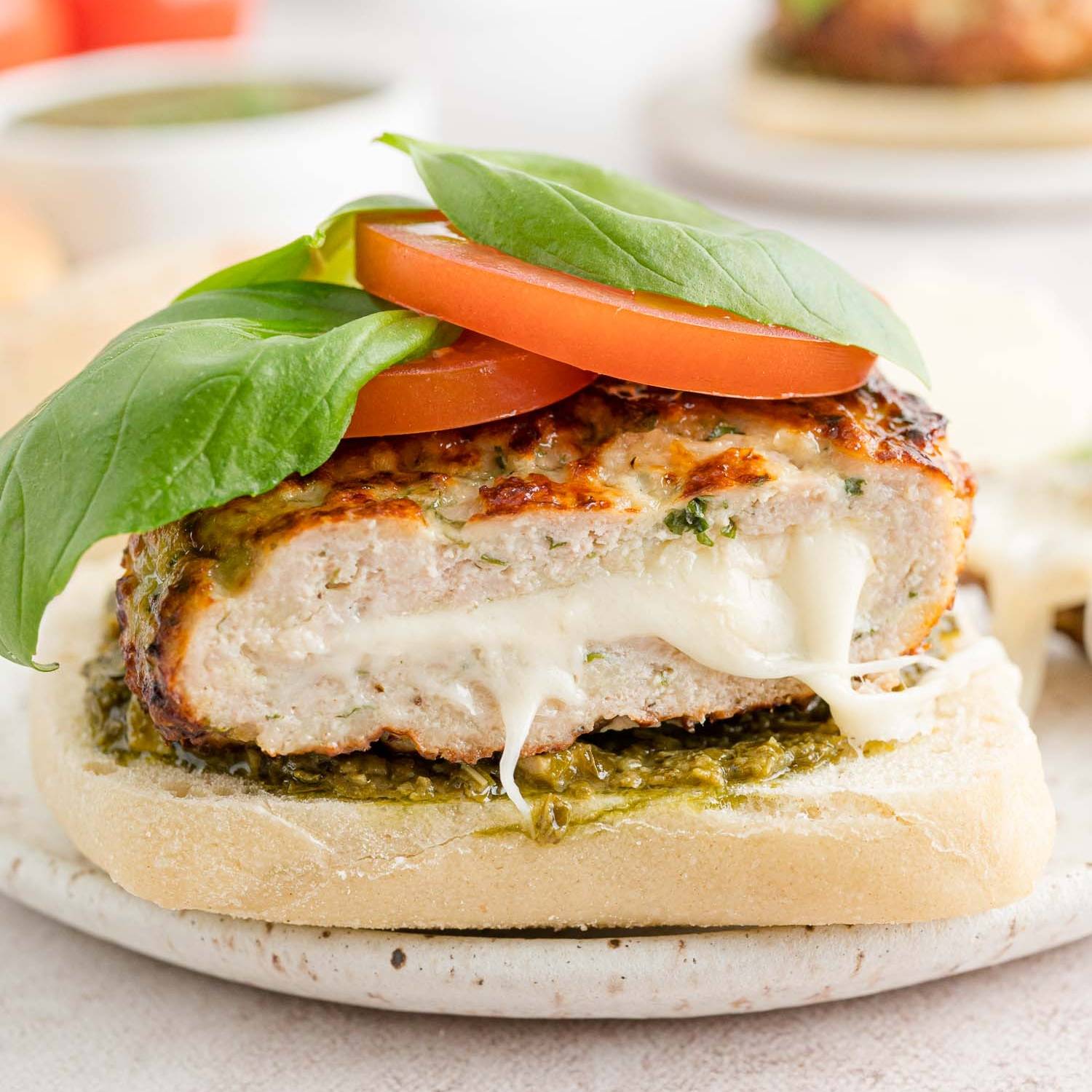Turkey burger on a ciabatta bun, burger is stuffed with cheese, and topped with tomato and basil.