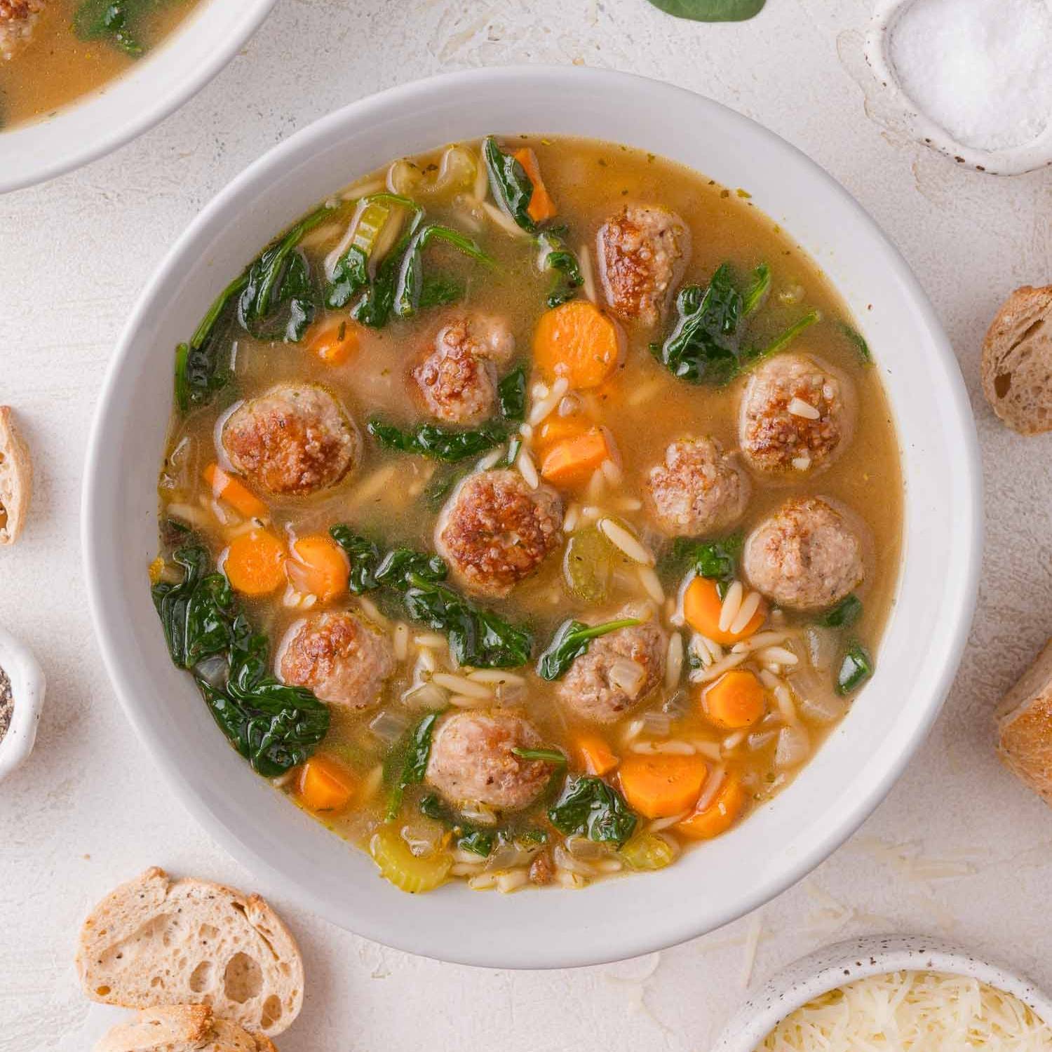 Meatball soup with orzo, carrots, and spinach in a white bowl.