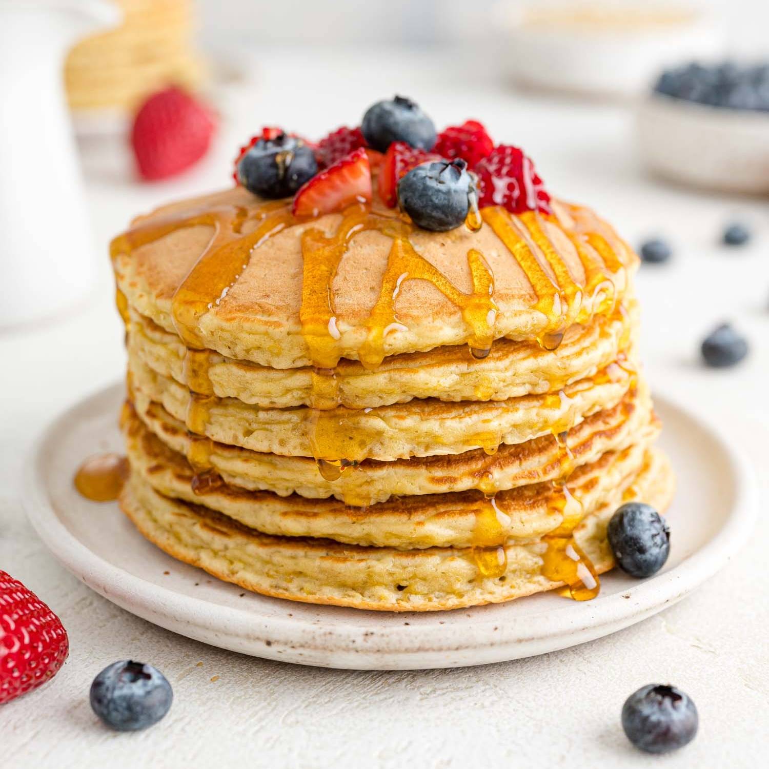 Stack of quinoa pancakes with maple syrup and fresh berries.
