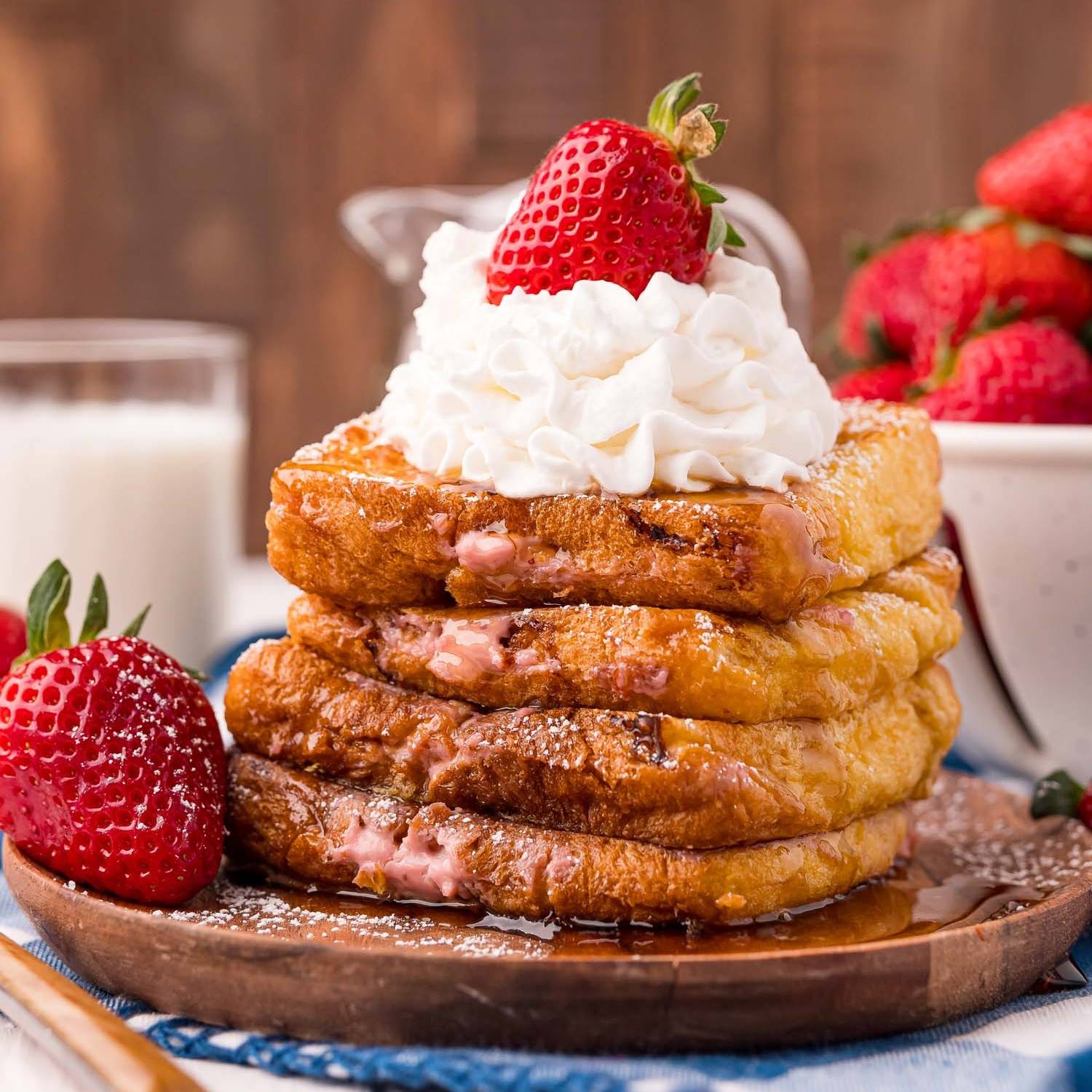 Four pieces of stuffed french toast in a stack topped with whipped cream and a strawberry.