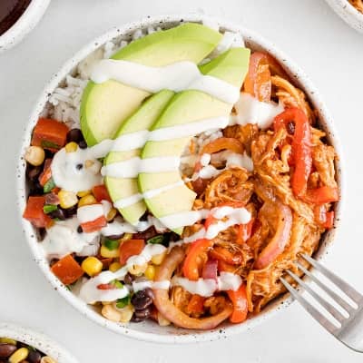 BBQ chicken bowl with rice, avocado, chicken, peppers and onions, black beans, and white sauce.
