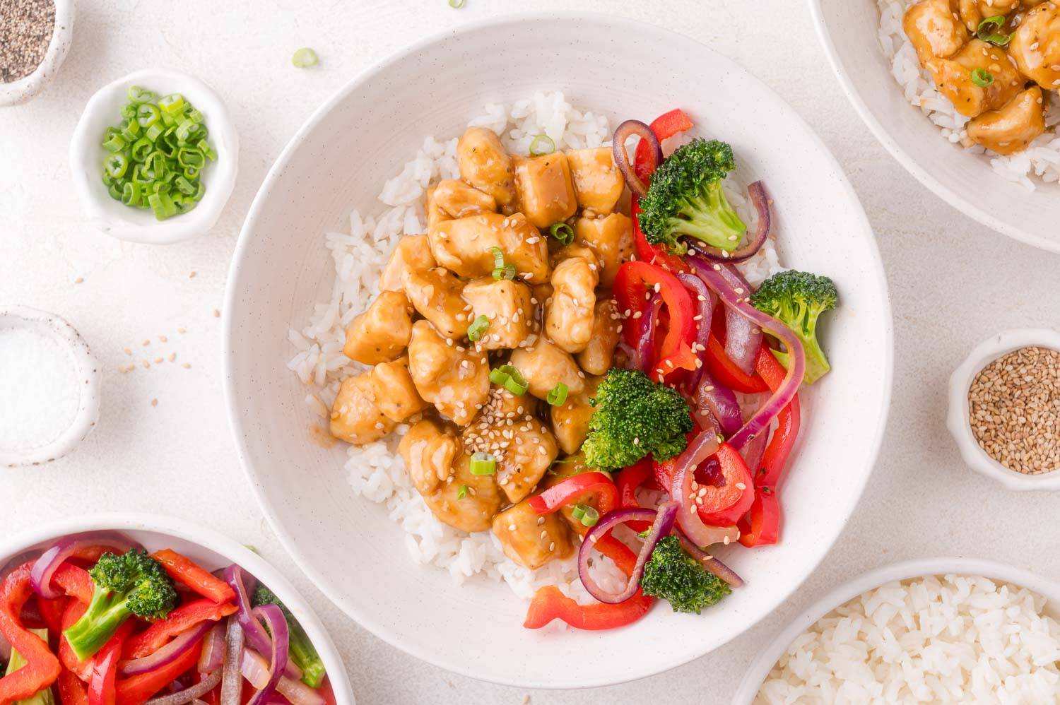 Teriyaki chicken and vegetables on rice in a white bowl.