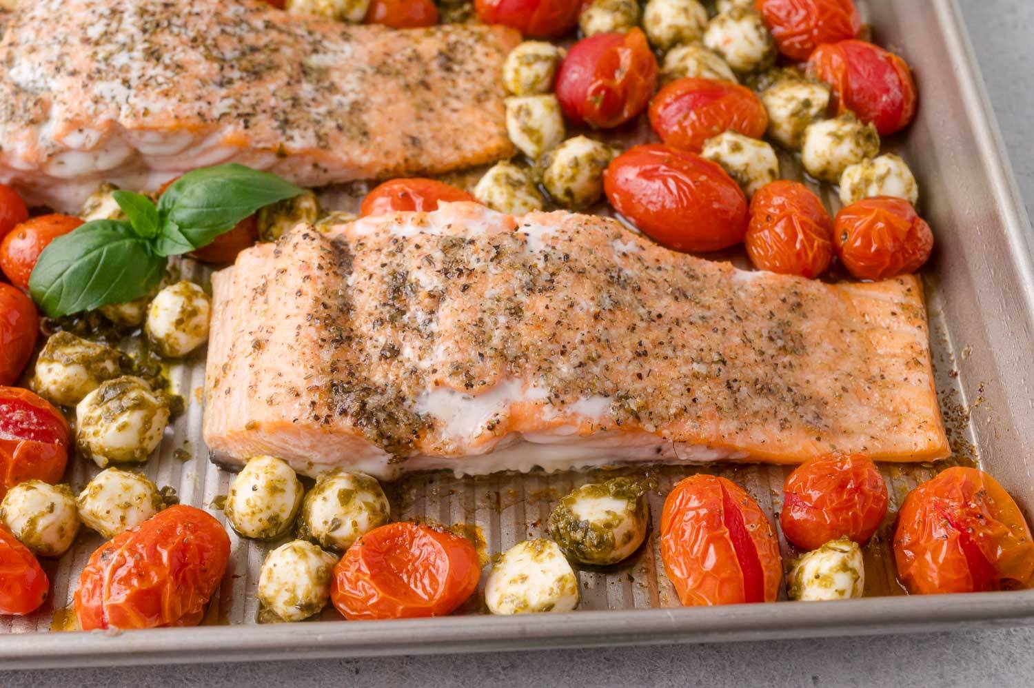 Salmon on a sheet pan with pesto coated mozzarella and roasted tomatoes.