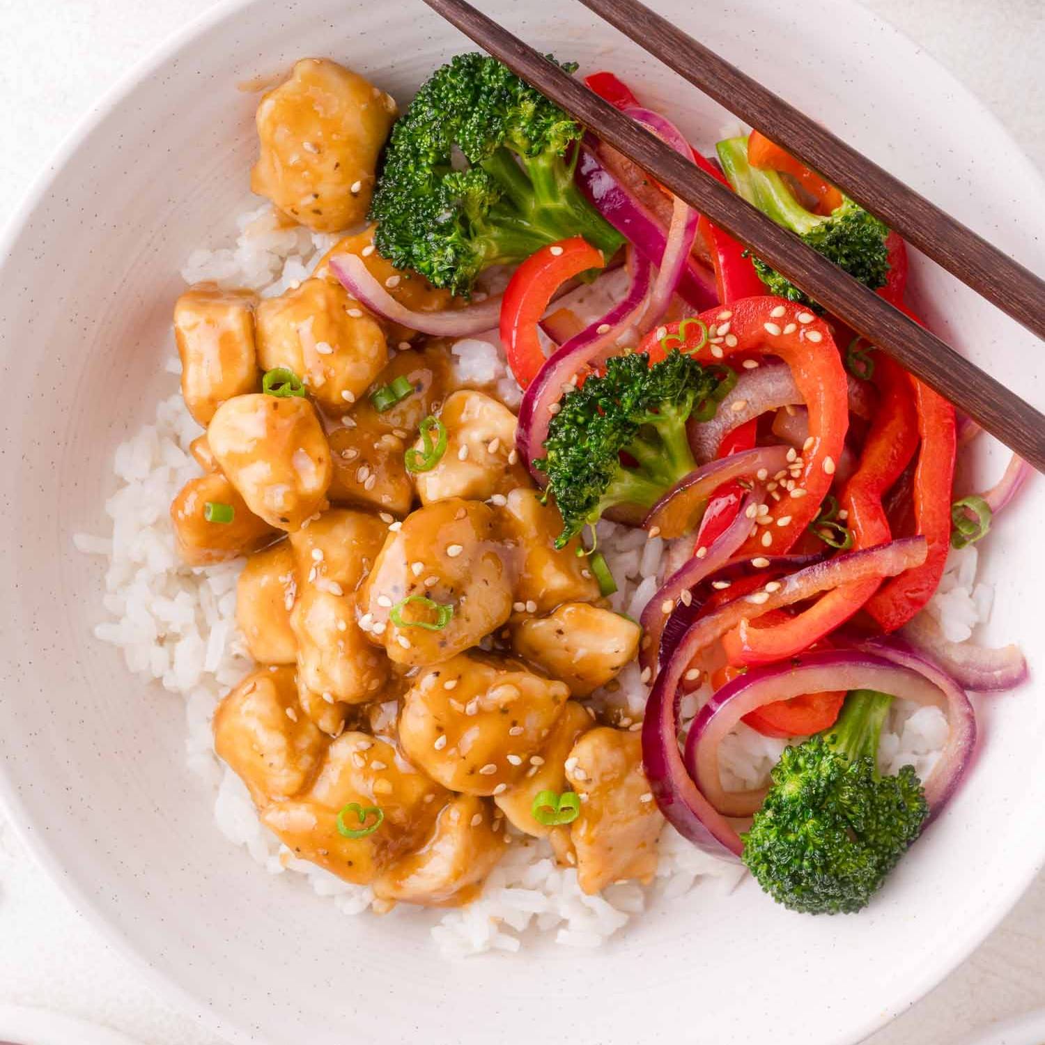 Teriyaki chicken and vegetables served over rice, in a white bowl.