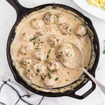 Swedish meatballs in a black skillet, one being scooped out with a large spoon.