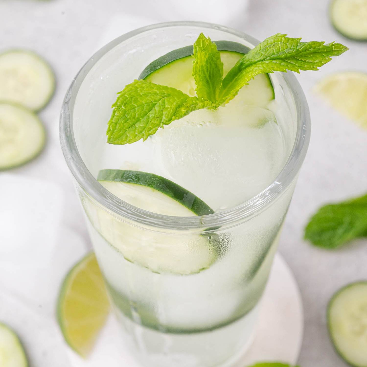 Clear drink in tall glass with cucumbers and mint.