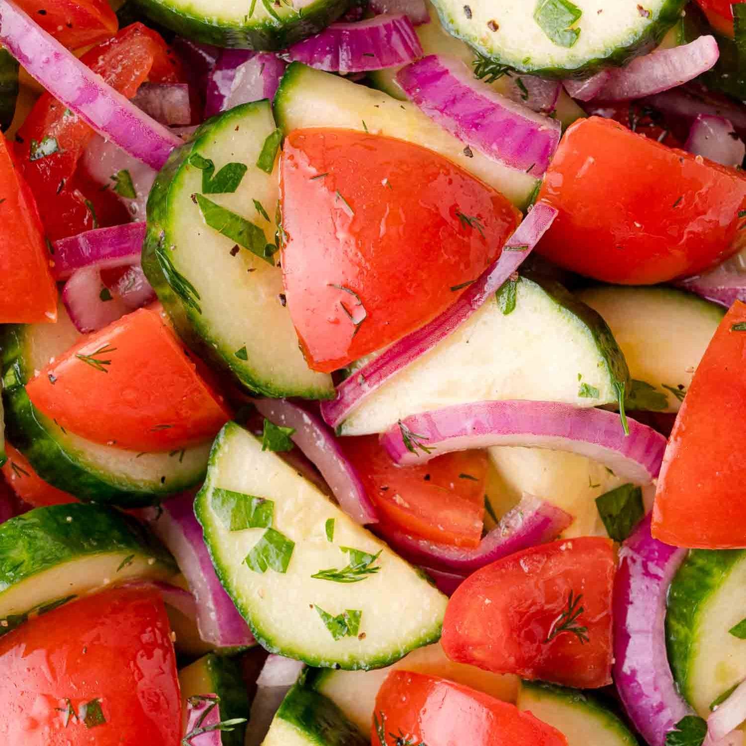 Close up of cucumbers, tomatoes, and red onions with fresh herbs.