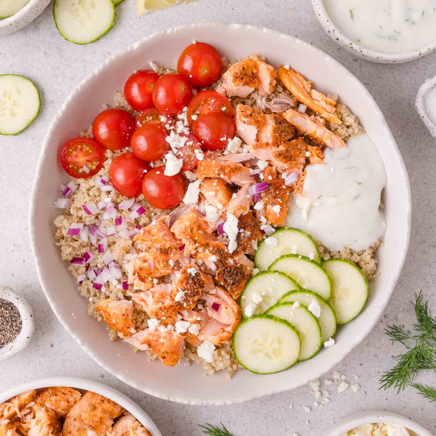 Flaked salmon in a bowl with rice, tomatoes, cucumber, and yogurt sauce.