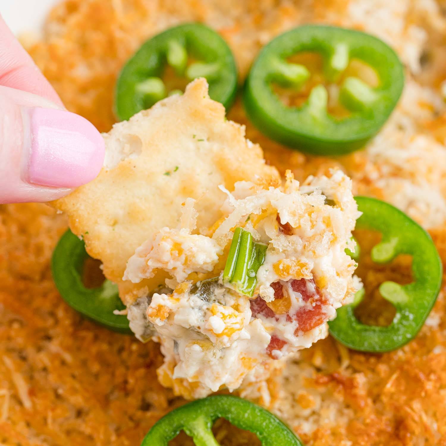 Cheesy dip with crispy topping, and fresh jalapeno slices on top, with a chip dipping into it.