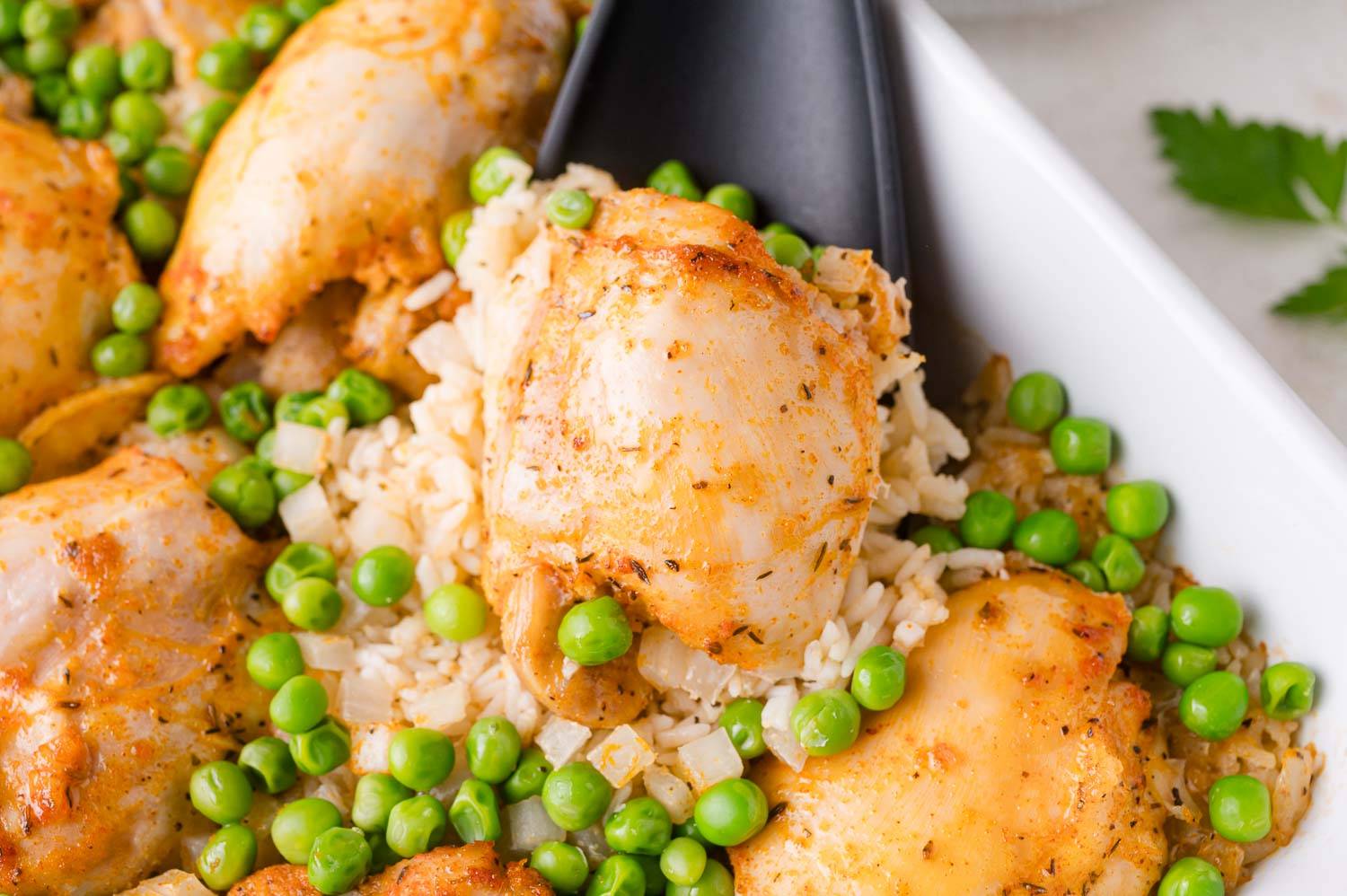Chicken, rice, and peas being scooped up with a black spoon.