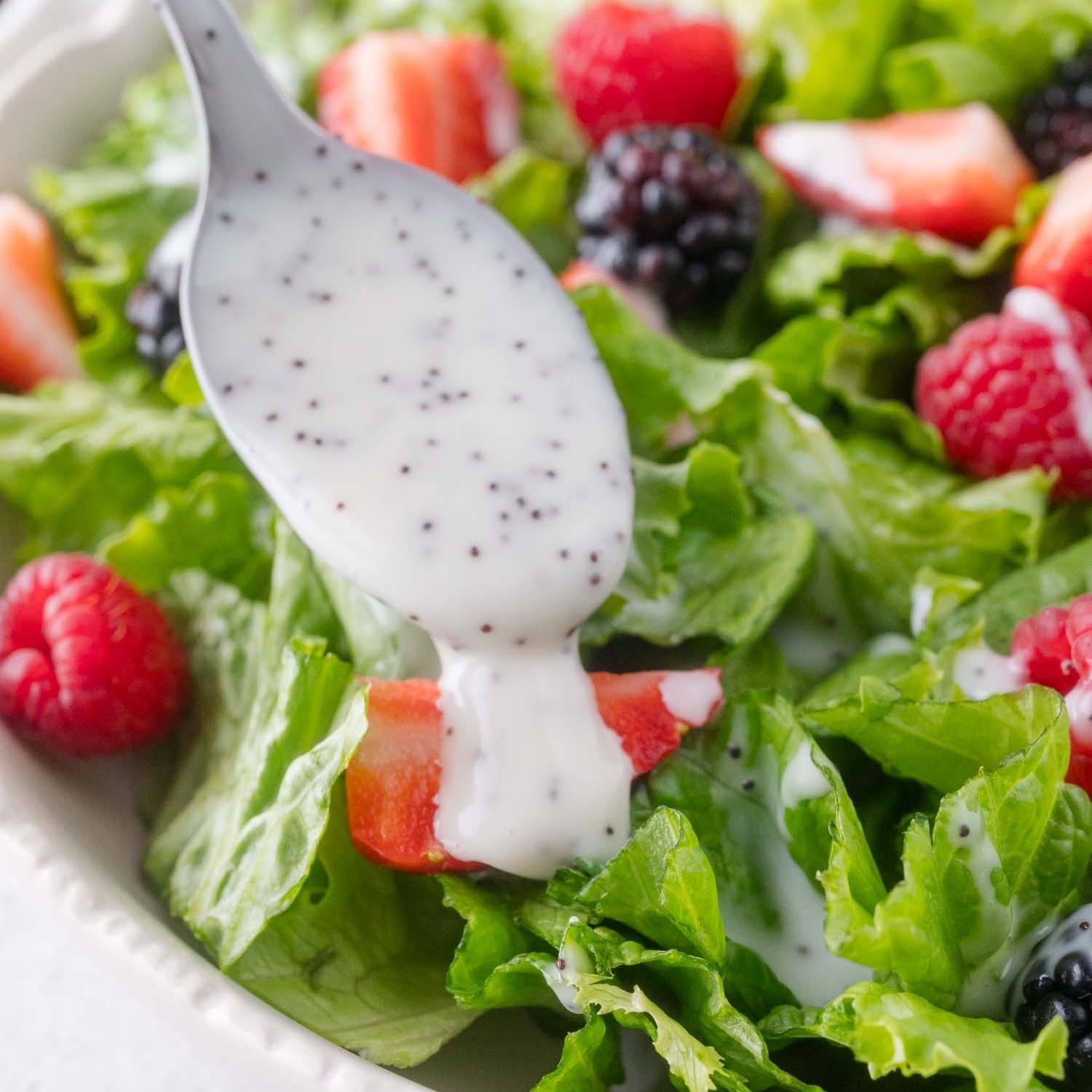 Poppy seed dressing being spooned onto a salad with lettuce and berries.