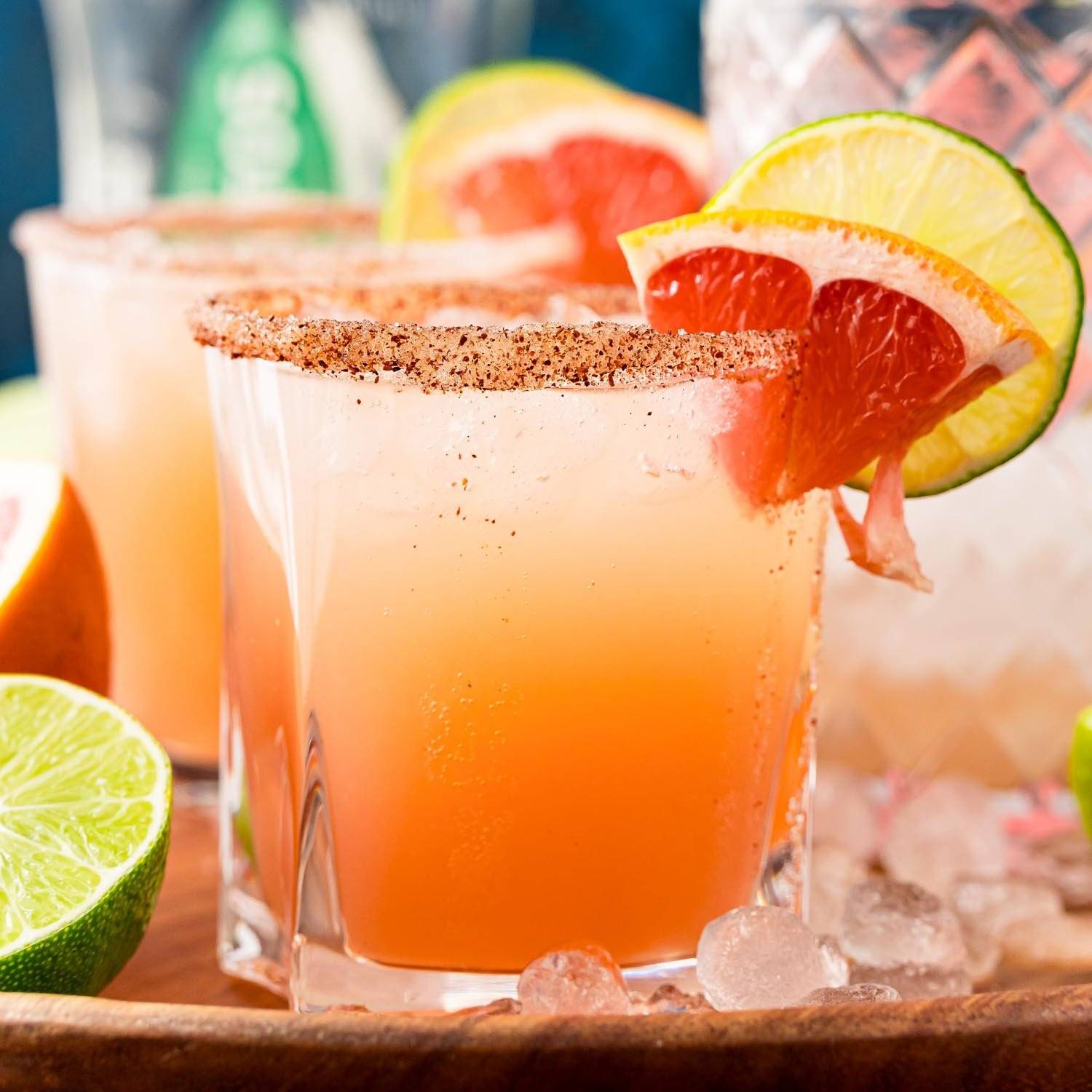A paloma in a short clear glass, garnished with grapefruit and lime slices. Another one is behind it.