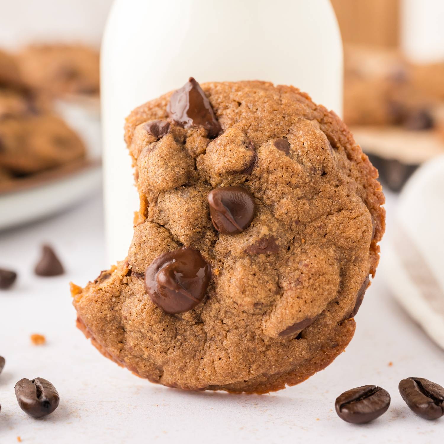 Cookie with chocolate chips and a bite out of it, standing next to a thing of milk.