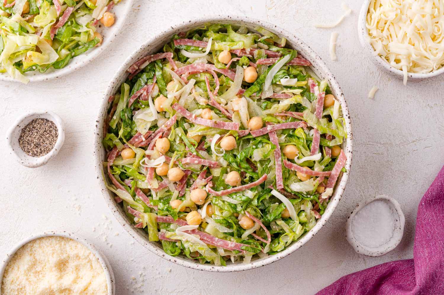 La scala chopped salad in a large bowl, topped with chickpeas, salami, and cheese.