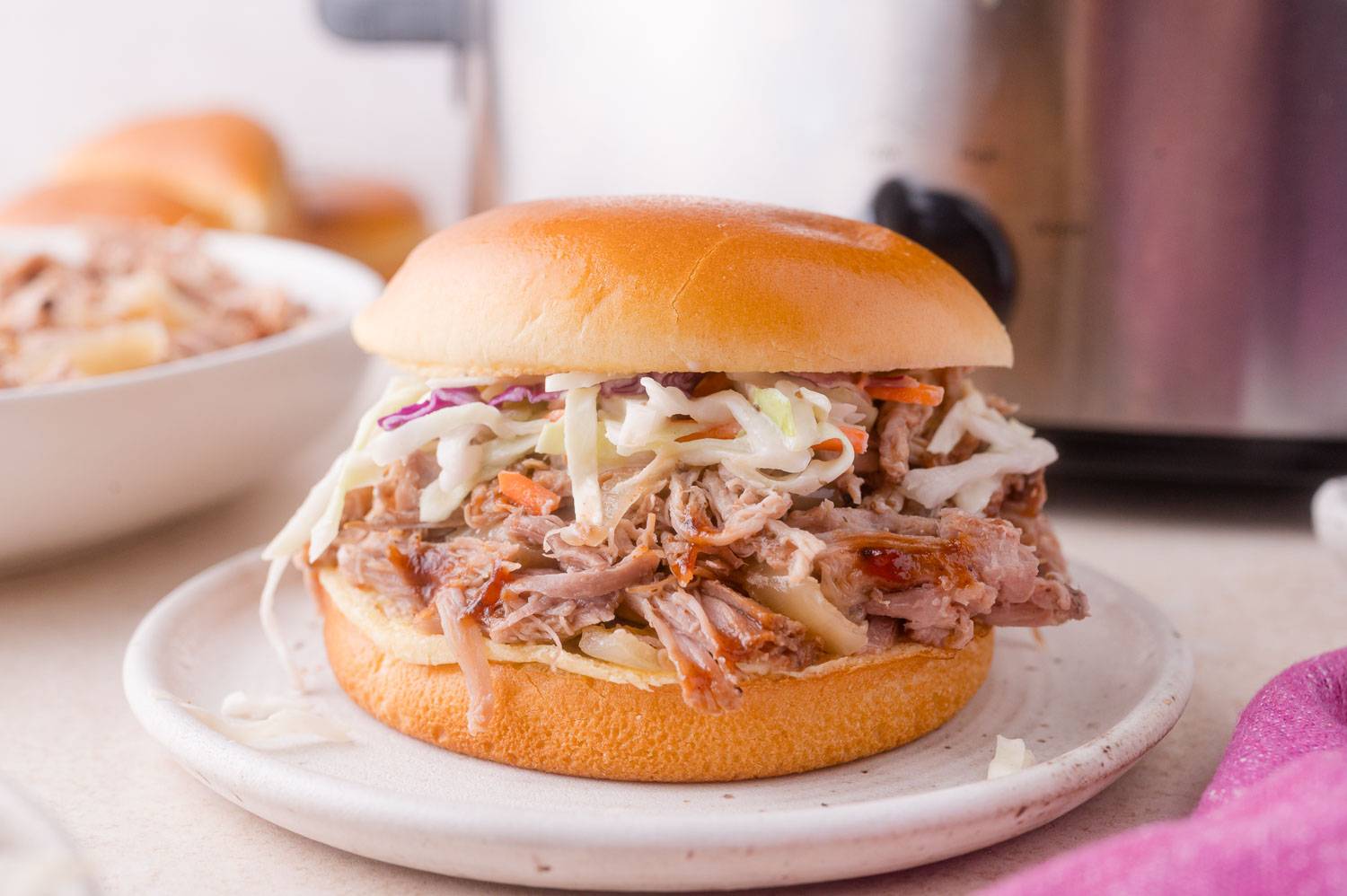 Apple cider pulled pork on a bun with coleslaw. A slow cooker is in the background.