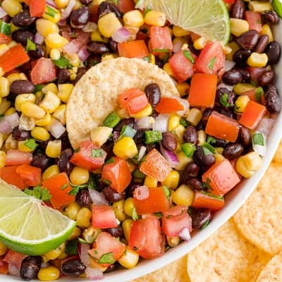 Balck bean corn salsa in a white bowl surrounded by chips.