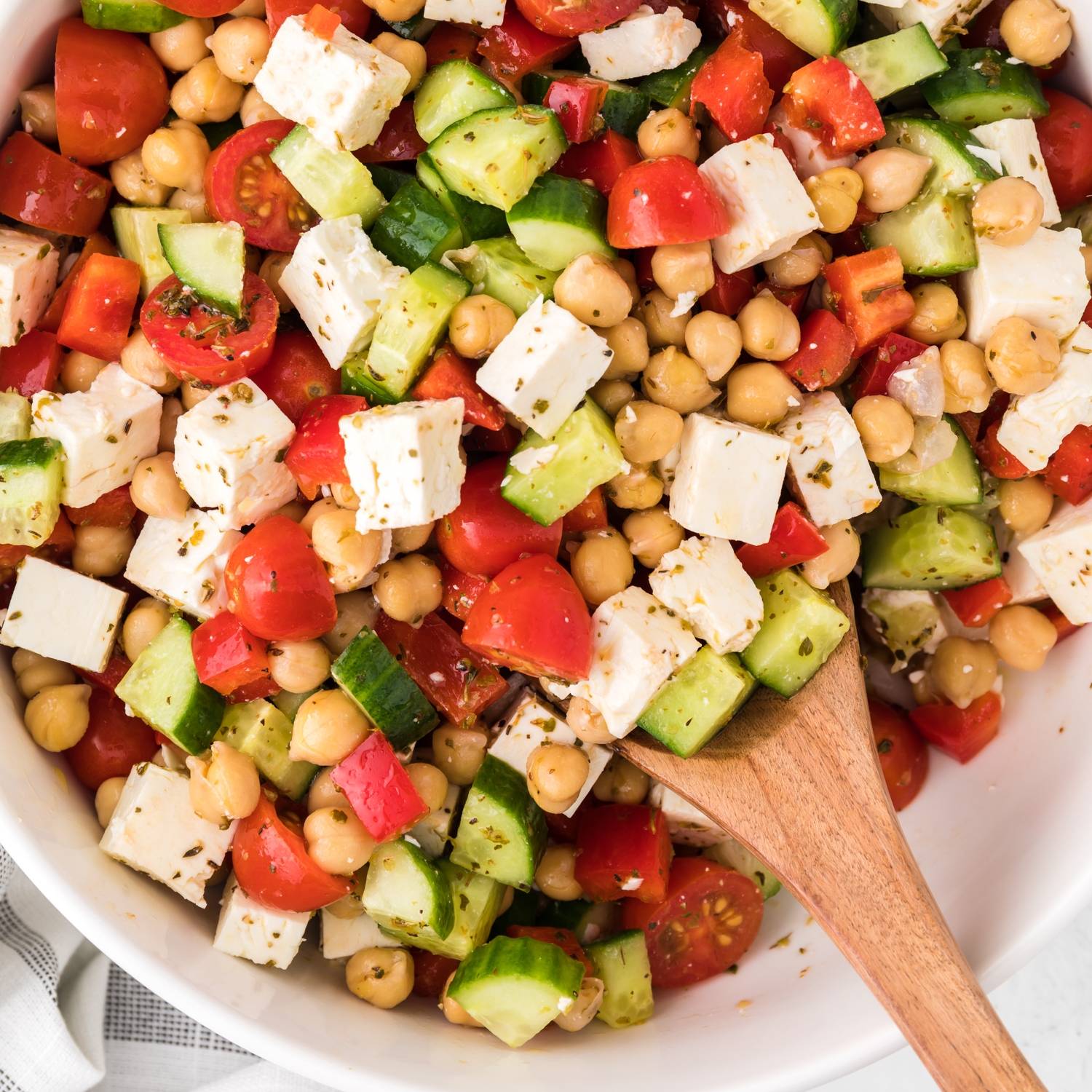 Greek chopped salad in a bowl with wooden spoon.