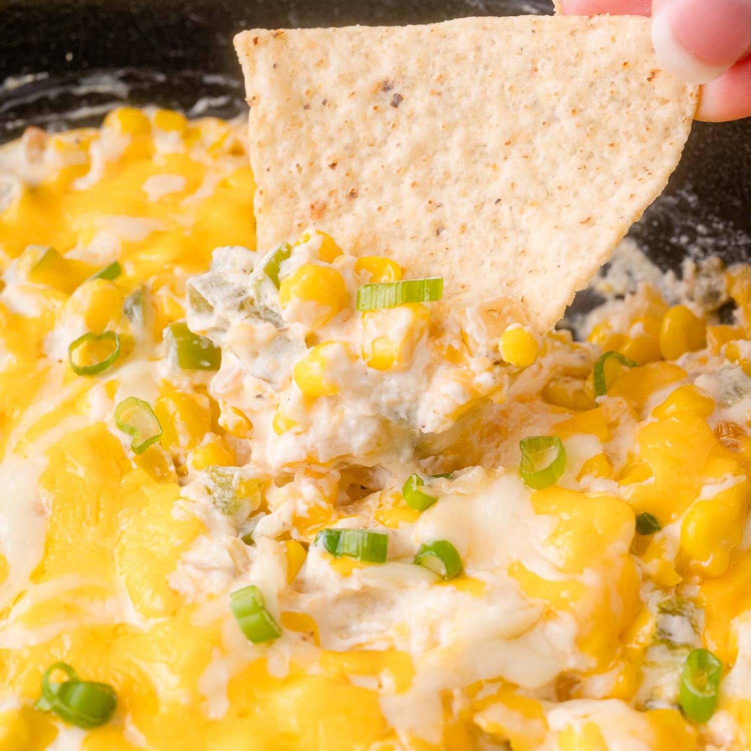 A chip dipping into a cheesy dip made with corn and alapeño.j
