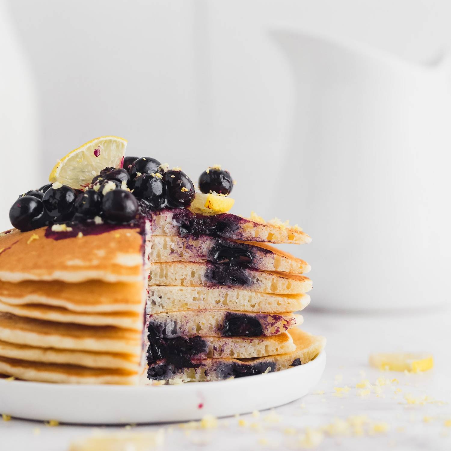 Stack of lemon blueberry pancakes, a wedge cut out to show inside of pancakes.