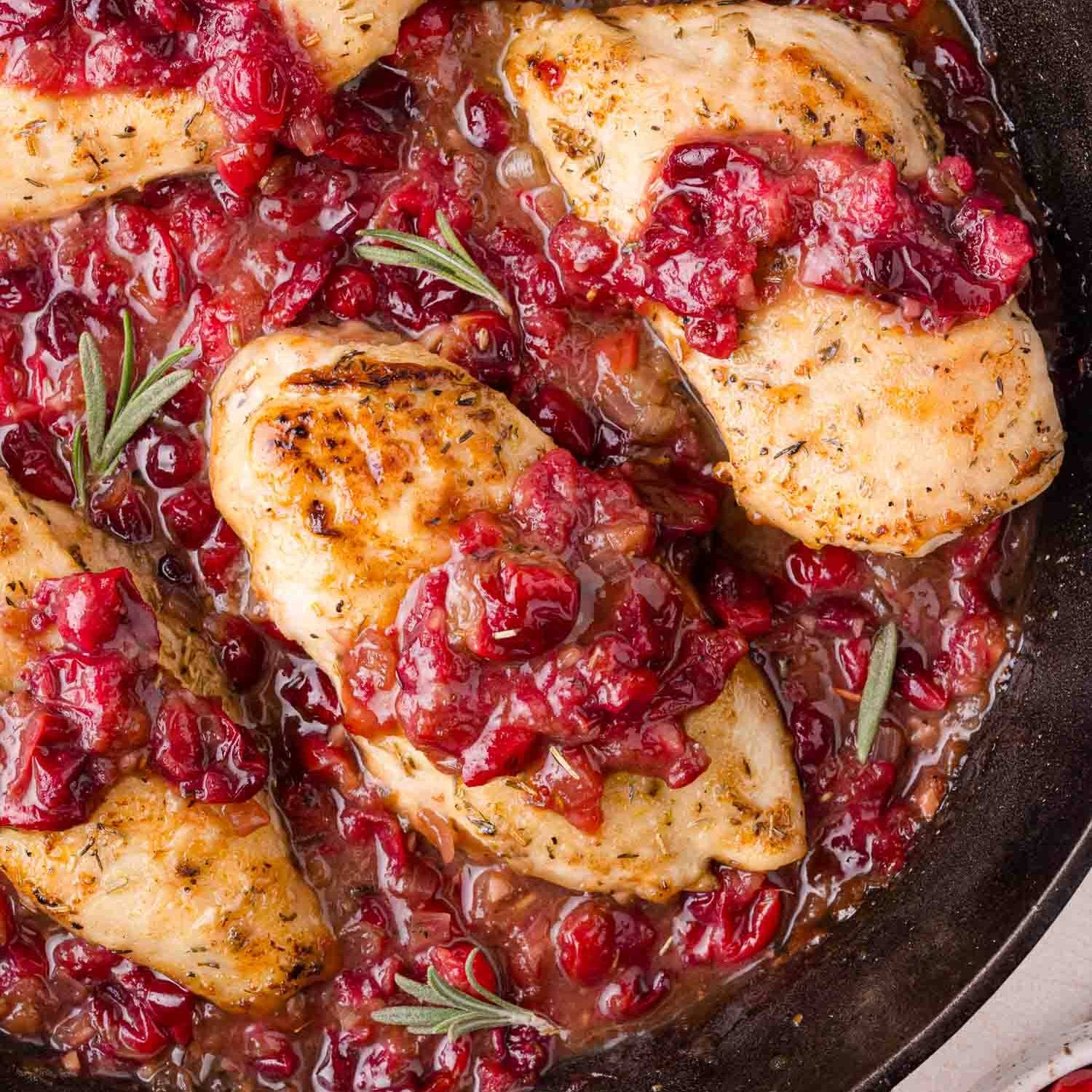 Chicken in a black skillet with cranberry sauce.