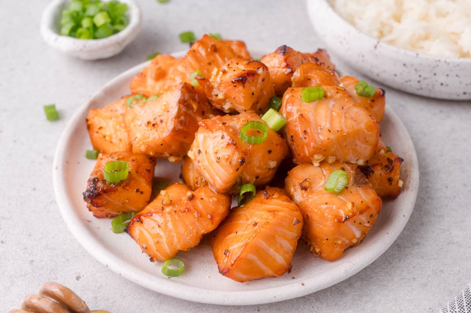 Honey garlic air fryer salmon bites on a plate, garnished with sliced green onions.