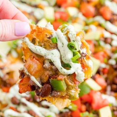 Vegetarian nacho being picked up with a hand.