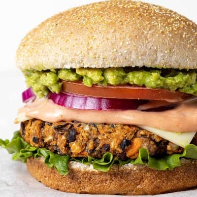 Black bean burger on a bun with burger sauce, cheese, lettuce, guacamole, onion, and tomato.