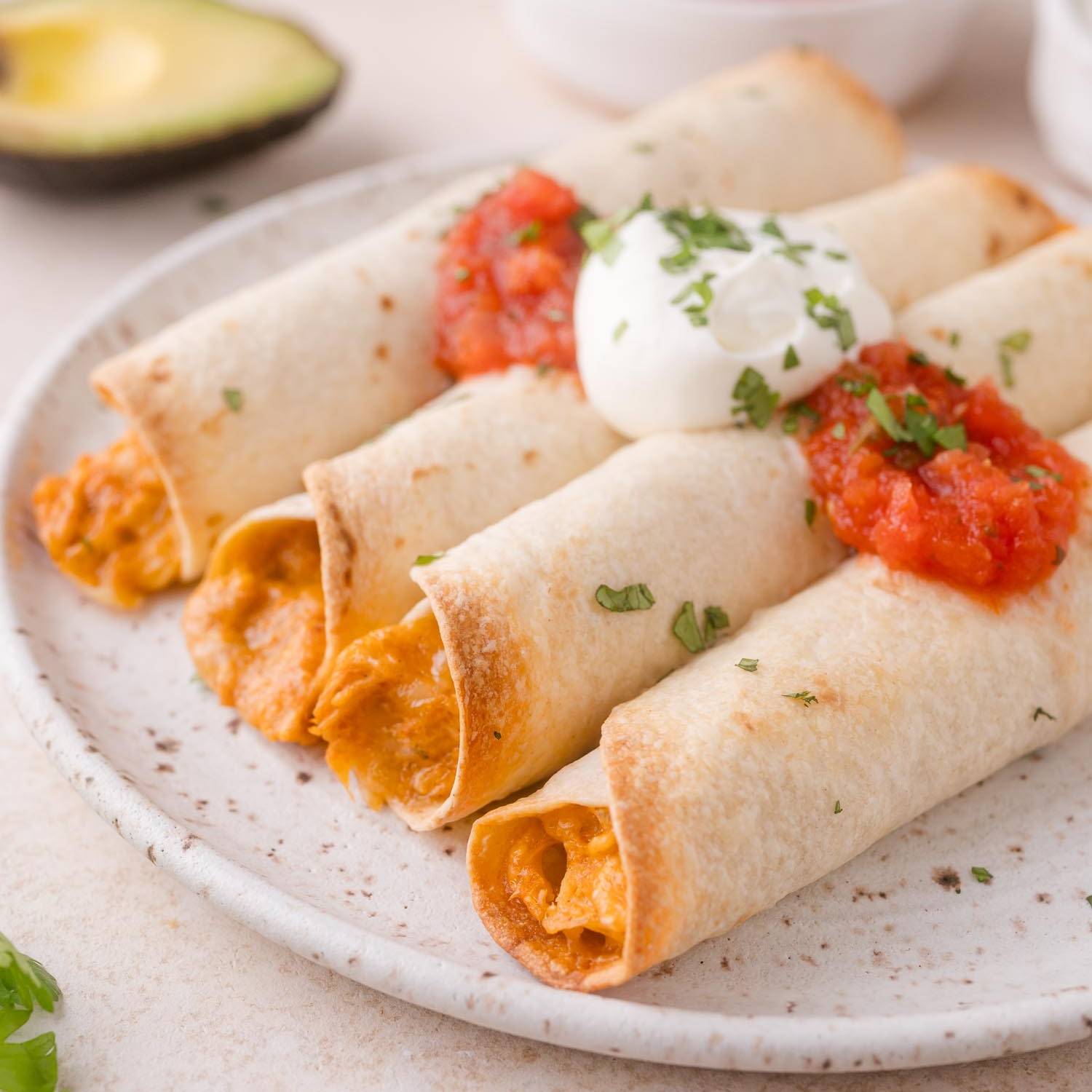 Four chicken taquitos on a plate, topped with salsa and sour cream.
