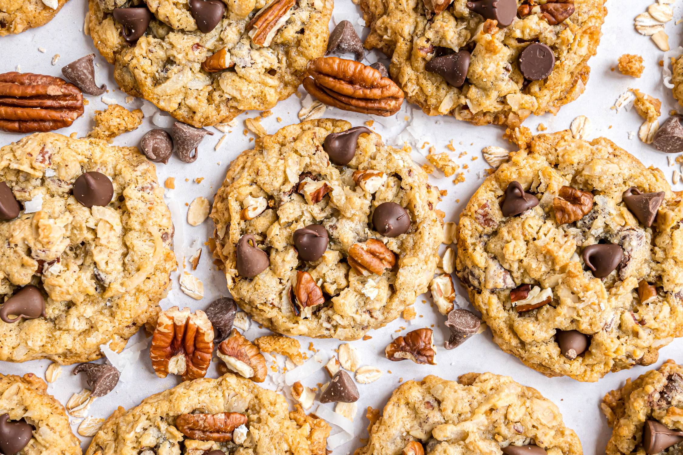 Cowboy cookies on white surface with chocolate chips and pecans.